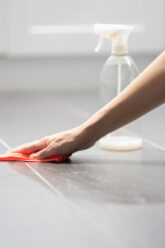 a-person-wiping-a-tiled-floor-with-a-red-cloth-beside-a-spray-bottle.