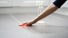 a-person-wiping-a-tiled-floor-with-a-red-cloth-beside-a-spray-bottle.